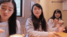 three girls are sitting at a table eating food and one of them is holding a bowl of food .