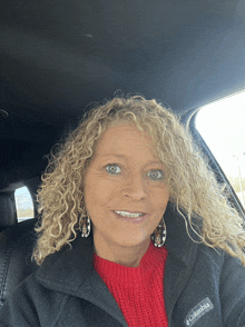 a woman wearing a black columbia jacket and a red sweater smiles for the camera