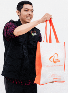 a man in a black vest is holding a bag that says zakat sinergi