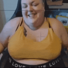a woman is sitting in a chair with her eyes closed and smiling while wearing a yellow sports bra .