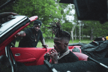 a man with dreadlocks sits in a red convertible