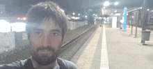 a man taking a selfie at a train station with graffiti on the wall behind him that says " a "