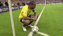 a soccer player is squatting down on the sidelines of a soccer field to kick a soccer ball .