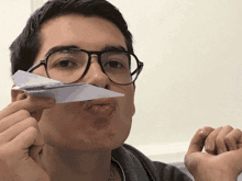 a young man wearing glasses is holding a paper airplane in front of his mouth