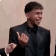 a man in a tuxedo and bow tie is waving his hand .