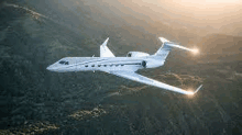 a small private jet is flying over a mountain range at sunset .