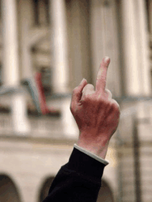 a person 's hand is making a middle finger gesture in front of a building