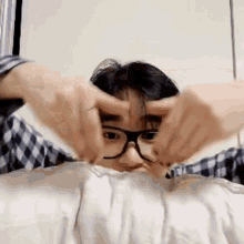 a young man wearing glasses is making a heart shape with his hands .