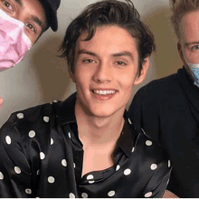 a man wearing a polka dot shirt is smiling for the camera while standing next to two other men .