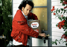 a man in a red jacket is opening a door with a box of badger milk on it