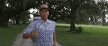 a man in a plaid shirt and a hat is running in a park .