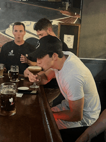 a man sitting at a bar drinking a martini with another man standing behind him