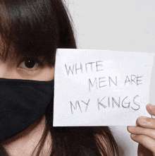 a woman wearing a black face mask holds up a sign that says white men are my kings