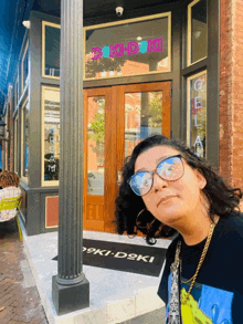 a woman wearing glasses stands in front of a storefront that says " doki doki " on it