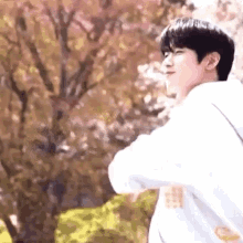 a young man in a white hoodie is standing in front of a cherry blossom tree in a park .