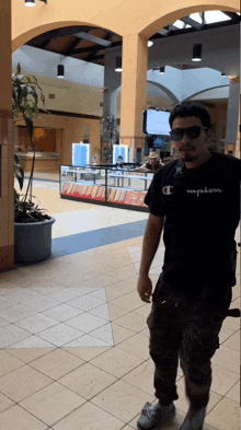 a man wearing sunglasses and a black champion shirt stands in a shopping mall