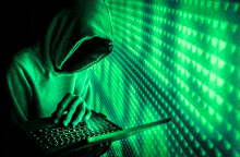 a person in a hoodie is typing on a laptop in front of a green background