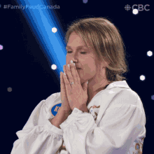 a woman covering her mouth with her hands in front of a blue background with the words family feud canada on it