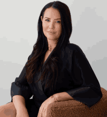 a woman wearing a black top sits on a brown chair