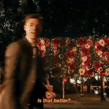 a man in a suit and tie is standing in front of a wall of flowers and trees .