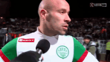 a bald man wearing a seat shirt is talking into a microphone