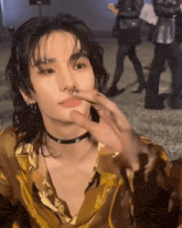 a young man with long hair and a choker is touching his face .