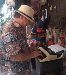 a man wearing a hat is typing on a typewriter with a shirt that has old cars on it