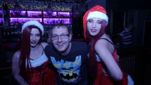 a man is posing for a picture with two women in santa hats in a bar .