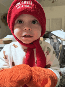 a baby wearing a red hat and scarf with the word columbia on it