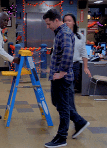 a man in a plaid shirt stands next to a blue and yellow ladder