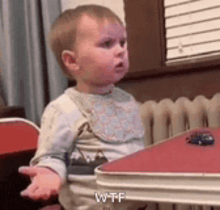 a baby is sitting at a table with a toy car and making a funny face .