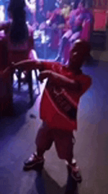 a young boy in a red shirt is dancing on a stage in a club .