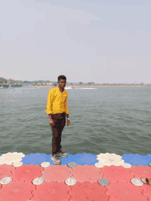 a young man in a yellow shirt is standing on a dock overlooking a body of water