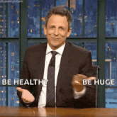 a man in a suit and tie is sitting at a table and says be healthy be huge .