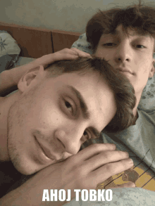 two young men laying on a bed with ahoj tobko written on the bottom right