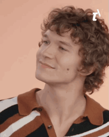 a young man with curly hair wearing a striped shirt is smiling