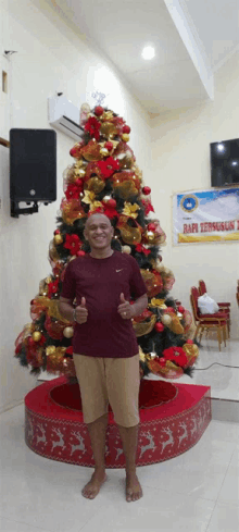 a man giving a thumbs up in front of a christmas tree in a room