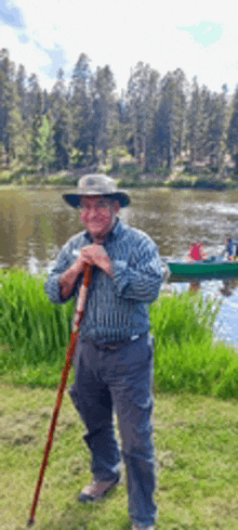 a man holding a cane in front of a lake with a boat in the background