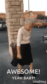 an elderly woman is dancing in a parking lot in front of a brick building .