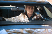 a man in a white jacket is driving a blue car