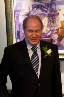 a man in a suit and tie stands in front of a painting with a flower on his lapel