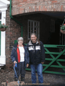 a man and a woman standing in front of a brick building with a green gate