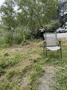 a child in a red white and blue shirt is standing next to a chair in the grass