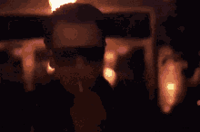 a man wearing sunglasses is lighting a cigarette in a dark room