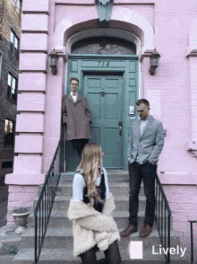 a group of people standing in front of a pink building with a green door that says ' lively ' on it