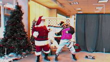 santa claus and a man in a pink jacket are dancing in front of a christmas tree at 30 fps