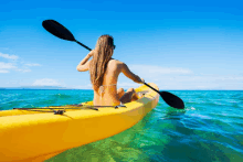 a woman in a bikini sits in a yellow kayak with a paddle