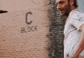 a man in a white shirt is standing in front of a brick wall with the word block written on it .