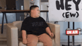 a boy sits in a chair in front of a sign that says hey