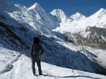 a man is standing on top of a snow covered mountain looking at the mountains .